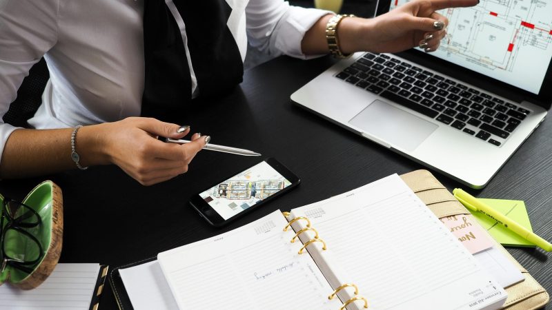A business professional working on real estate project plans using multiple devices in an office setting.